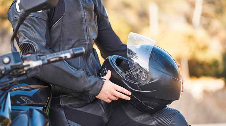 A man in a black leather jacket inspects a visored helmet.